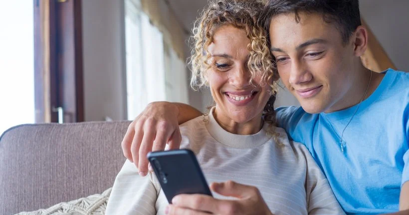 A teen and his mum look at a smartphone.