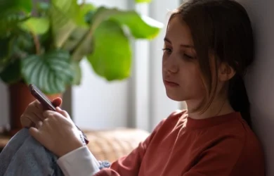 A girl sits with her phone with a sad expression.